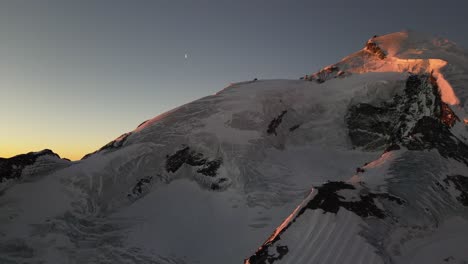 Luftaufnahme-Eines-Schneebedeckten-Und-Felsigen-Berges-In-Den-Alpen,-Wintersonnenaufgang,-Wunderschöne-Landschaft