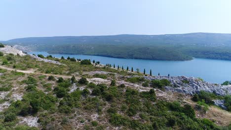 Aerial-Drone-Above-Forest-Hill-Road-of-Rakalj-Pula-Sea-Croatia,-Blue-Seascape-of-Green-Islands-in-Calm-Croatian-Turquoise-Water-Bay
