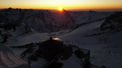 aerial-view-of-a-restaurant-on-top-of-the-alps-during-a-sunrise,-mountain-range