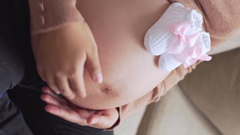 Woman-rubbing-her-pregnant-belly-with-pink-tiny-shoes-on-top,-close-up-vertical