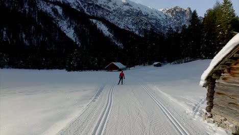 Person-in-red-dress-skiing-on-snowy-terrain-between-wooden-houses