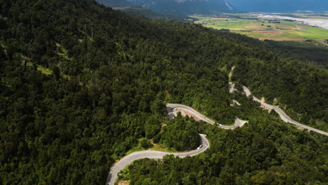 Aerial-view-of-vehicles-driving-through-curvy-road-in-forest-landscape