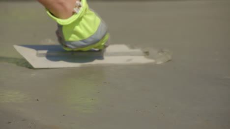 Hand-of-worker-plastering-cement-floor-with-yellow-glove,-slow-motion