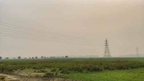 High-voltage-power-lines-stretch-along-Bangladesh-rural-landscape,-pan-left-view