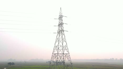 Slow-pull-back-of-electricity-pylon-tower-on-hazy,-misty-Bangladesh-countryside-sunrise-skyline