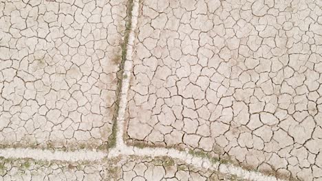 Dry-cracked-drought-fractured-agricultural-land-sections-aerial-view-rotating-descent-above-barren-damaged-landscape