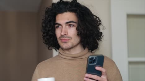 Coffee-and-Technology:-Spanish-Young-Man-with-Curly-Hair-Checking-His-Phone-in-Stylish-Turtleneck