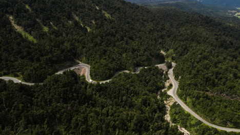 Aerial-shot-of-a-curvy-highway-among-dense-mountainous-forest-of-West-New-Zealand