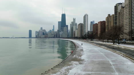 People-walking-on-the-Concrete-Beach-under-tall-buildings-of-Gold-Coast,-Chicago,-USA---Aerial-view