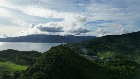 Rotating-Aerial-View-of-lush-jungle-covered-mountain-amidst-province-of-Catanduanes-with-small-barangay-town-and-idyllic-ocean-bay-in-the-background