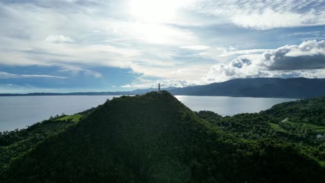 Breathtaking,-High-contrast-Aerial-View-of-lone-white-lighthouse-sitting-atop-peak-of-rainforest-covered-hill-in-the-island-of-Catanduanes,-Philippines