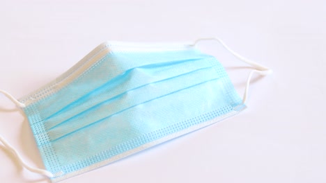 hand-in-a-blue-medical-glove-picking-up-a-blue-cotton-face-mask