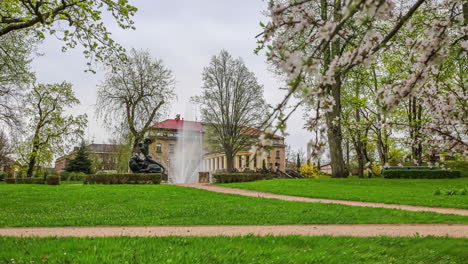 Spring-cherry-blossoms-and-a-water-fountain-in-a-park-in-Cesis,-Latvia---sliding-motion-time-lapse