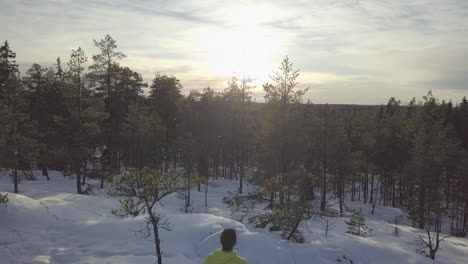 Winter-hiking-man-on-mountain-top-in-Ice-cold-Arctic-forest-watching-sunset-view
