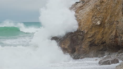 Intense-waves-hitting-cliff-rocks-in-slow-motion,-splashing-aqua-blue-sea-water