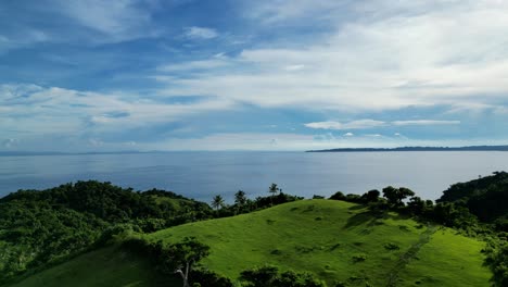 Aerial-footage-of-lush-green-grass-on-an-island-mountain-top-with-soft-sunlight-casting-long-shadows,-while-the-ocean-provides-a-stunning-background