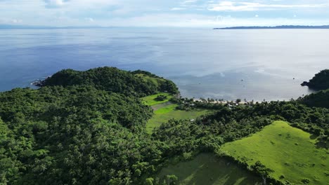 A-stunning-aerial-birds-eye-view-of-Catanduanes,-a-Philippine-island-surrounded-by-ocean,-hills-covered-in-grass-and-trees