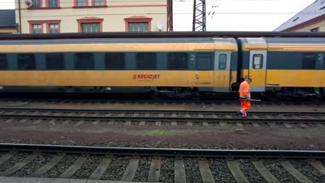 Train-engineer-in-a-reflective-orange-vest-walks-along-the-tracks-in-the-station