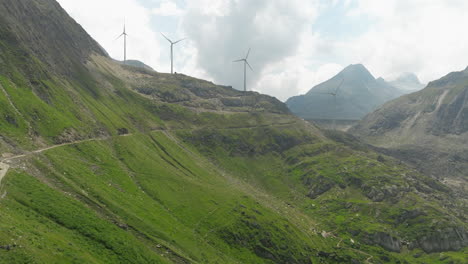 Grimsel-Pass-Mountain-Road-Con-Turbinas-Eólicas-En-El-Fondo-En-Los-Alpes-Berneses,-Suiza