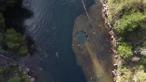 Top-aerial-view-over-river-and-people-swimming-and-relaxing-in-natural-rock-water-pond-at-river-banks,-captured-at-Patagonia,-Argentina,-South-America