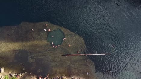 Top-aerial-view-over-river-and-people-swimming-and-relaxing-in-natural-rock-water-pond-at-river-banks,-captured-at-Patagonia,-Argentina,-South-America-during-sunshine-day-and-nice-weather