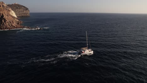 Vista-Aérea-De-La-Navegación-En-Catamarán-En-El-Mar-Egeo-Cerca-De-La-Costa-De-La-Isla-De-Santorini,-Grecia