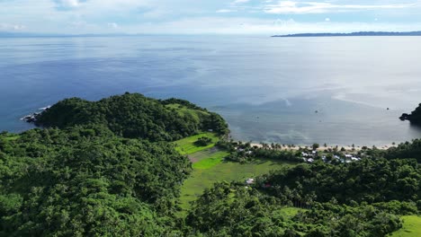 High-Angle-Establishing-Drone-shot-of-Island-Paradise,-Catanduanes,-with-lush-rainforest-covered-hills-and-beachfront-town-facing-idyllic,-calm-ocean-waters