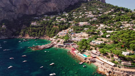 A-dynamic-aerial-shot-on-a-sunny-summer-day-approaching-the-beautiful-beaches-of-Marina-Piccola-on-Capri,-a-famous-island-that-is-a-popular-luxury-vacation-destination-in-Italy-along-the-Amalfi-Coast