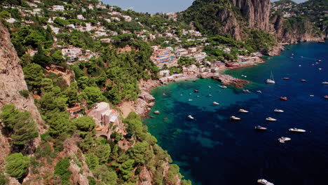 An-epic-aerial-shot-approaching-Marina-Piccola-beaches-past-the-stunning-cliffs-of-Capri,-a-famous-island-that-is-a-popular-luxury-vacation-destination-in-Italy-along-the-Amalfi-Coast