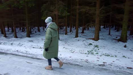 A-young-girl-in-warm-clothes-walks-along-a-snowy-path-in-winter-in-the-forest