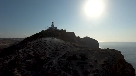 Racing-FPV-drone-flying-around-the-lighthouse-of-Santorini,-Greece-and-diving-over-cliffs