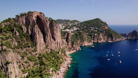 Eine-4K-Luftaufnahme-Von-Booten-Und-Yachten-Im-Meer-Rund-Um-Die-Hohen-Klippen-Und-Die-Atemberaubende-Küste-Von-Capri,-Einer-Berühmten-Insel,-Die-Ein-Beliebtes-Luxusurlaubsziel-In-Italien-An-Der-Amalfiküste-Ist
