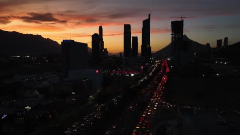 Luftaufnahme-über-Den-Verkehr,-In-Richtung-Silhouettenwolkenkratzer-In-San-Pedro-Garza-Garcia,-Monterrey,-Farbenfrohe-Abenddämmerung-In-Mexiko