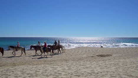 six-People-riding-horses-on-the-beach-mid-day,-sunny,-with-blue-sky