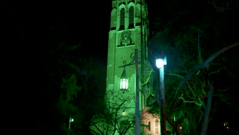 Beaumont-Tower-on-the-campus-of-Michigan-State-University-lit-up-at-night-in-green-in-honor-of-the-victims-of-the-February,-2023-mass-shooting-with-close-up-video-tilting-up-with-lamp