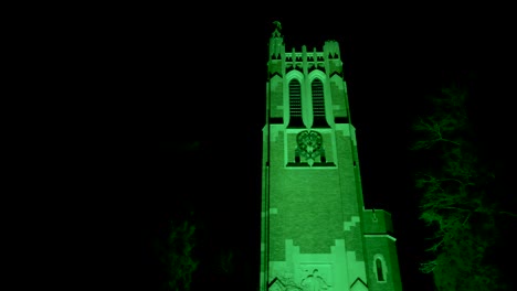 Beaumont-Tower-on-the-campus-of-Michigan-State-University-lit-up-at-night-in-green-in-honor-of-the-victims-of-the-February,-2023-mass-shooting-with-close-up-video-panning-left-to-right
