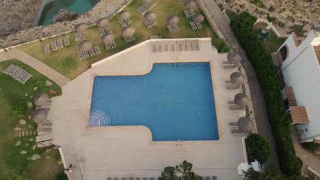 Aerial-rising-view-above-Mallorca-holiday-resort-clear-blue-pool-with-sun-loungers