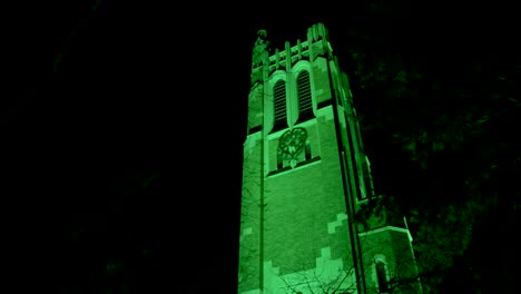Beaumont-Tower-on-the-campus-of-Michigan-State-University-lit-up-at-night-in-green-in-honor-of-the-victims-of-the-February,-2023-mass-shooting-with-video-close-up-walking-through-trees