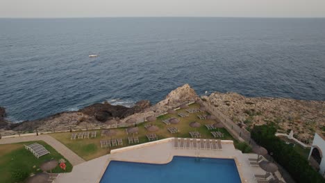 Drohne-Fliegt-Bei-Sonnenuntergang-über-Einem-Privaten-Resort-Auf-Mallorca,-Spanien,-Mit-Luxusanwesen-Am-Rande-Einer-Klippe-Und-Leerem-Pool