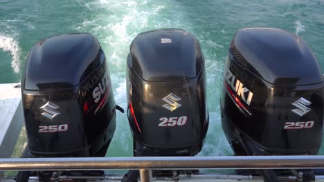 3-black-Suzuki-outboard-engines-on-back-of-speedboat,-reduced-power,-glinting-in-sunlight