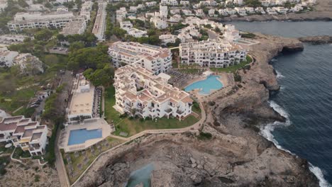 Establishing-aerial-view-flying-over-Mallorca-holiday-resort-on-Mediterranean-coastal-cliff-edge