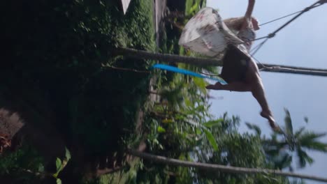 Vertical-FPV-Rotating-slowmotion-shot-of-a-beautiful-blond-woman-spreading-her-arms-and-enjoying-the-swing-set-in-the-tropical-nature-of-Bali