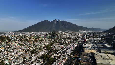 Aerial-view-over-the-cityscape-towards-the-Cerro-de-la-silla-mountain,-in-sunny-Monterrey,-Mexico