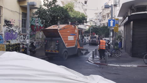 Ein-Arbeiter-In-Einer-Leuchtend-Orangefarbenen-Uniform-Bedient-Einen-Großen,-Leistungsstarken-Stadtreinigungswagen-Und-Sprüht-Kräftige-Wasserstrahlen,-Um-Schmutz-Und-Dreck-Schnell-Von-Den-Straßen-Zu-Entfernen