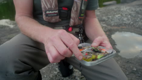 Pescador-Con-Mosca-Mostrando-Diferentes-Moscas-En-Su-Caja-De-Aparejos