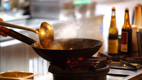 Chef-stir-frying-food-at-a-restaurant-kitchen,-faceless-professional-cook-cooking-seen-from-the-side,-bokeh