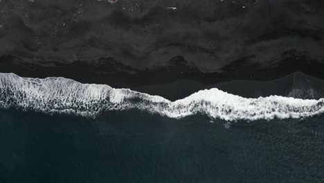 Top-down-slowmotion-drone-shot-of-waves-rooling-on-black-sand-beach-in-Indonesia