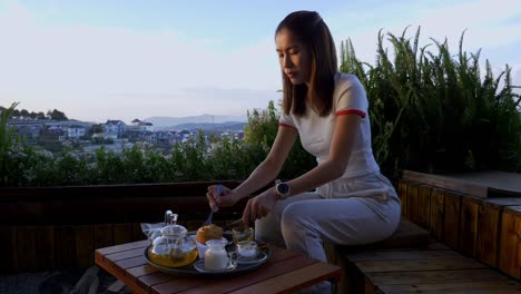 Asian-woman-eating-muffin-on-deck-with-beautiful-town-view,-Da-Lat