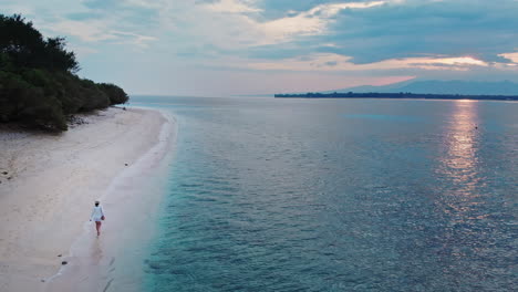 Beautiful-woman-walking-on-sandy-beach-and-turquoise-sea-at-dawn