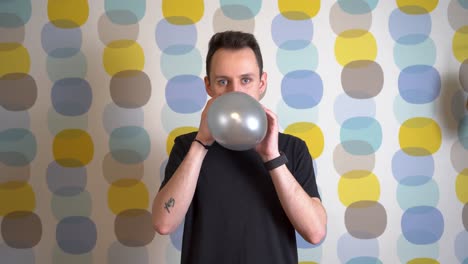 Young-Man-Blowing-a-Purple-Balloon-Against-Colorful-Background